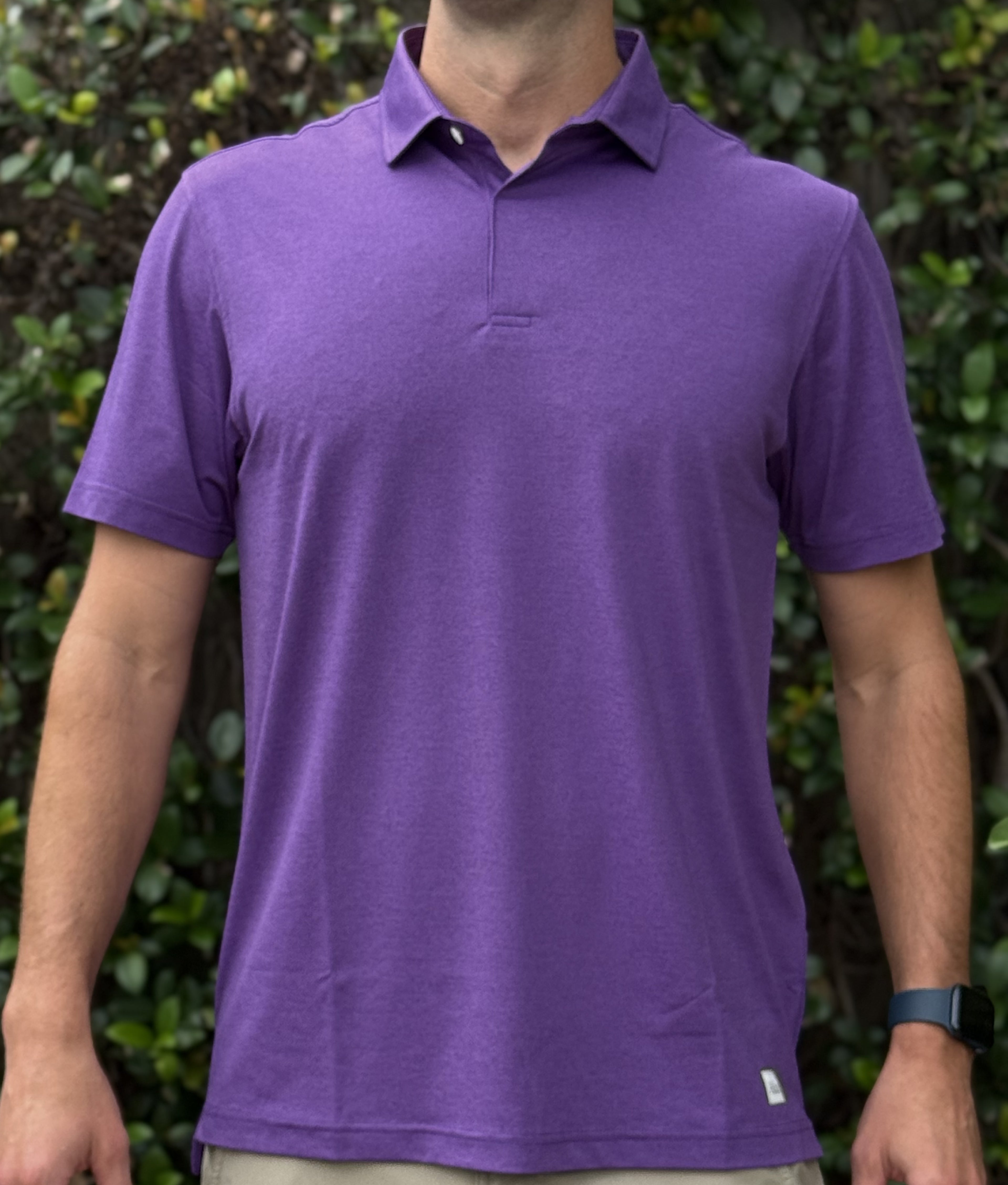 Person wearing a purple polo shirt with a green leafy background