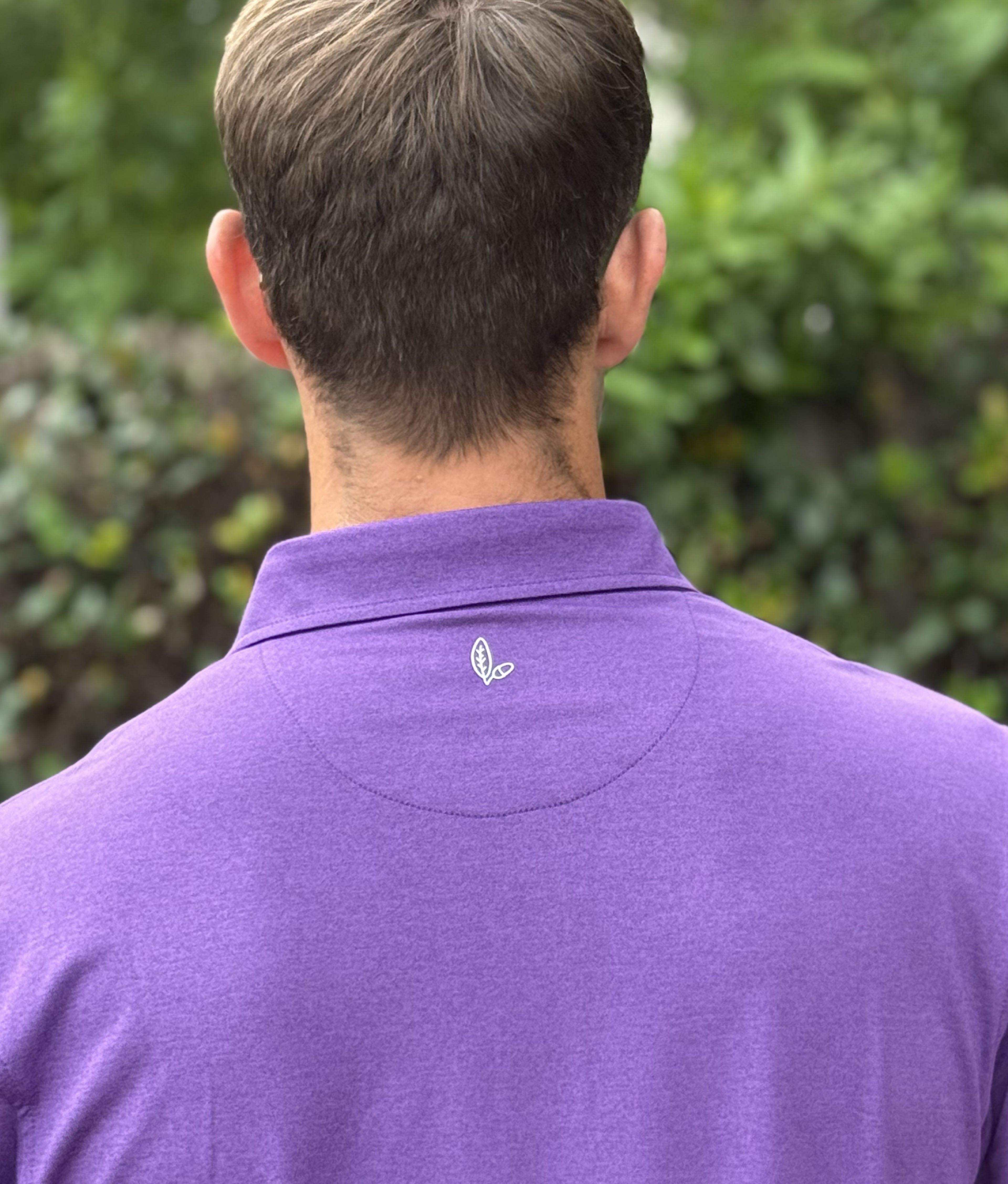 Person wearing a purple polo shirt with Alon's leaf and acorn logo beneath the collar.