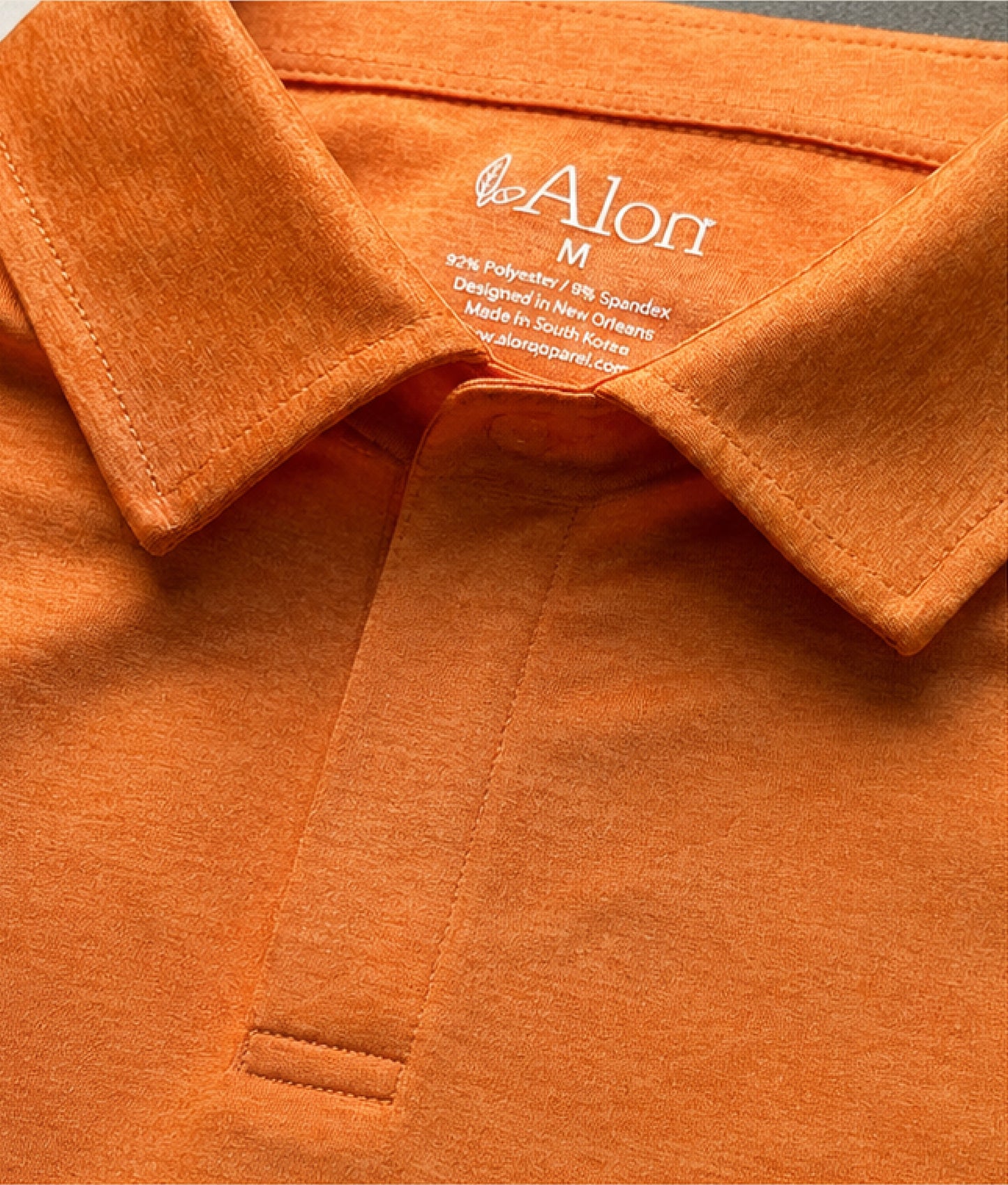 Close-up of an orange polo shirt with a clean placket with hidden magnets instead of buttons. 