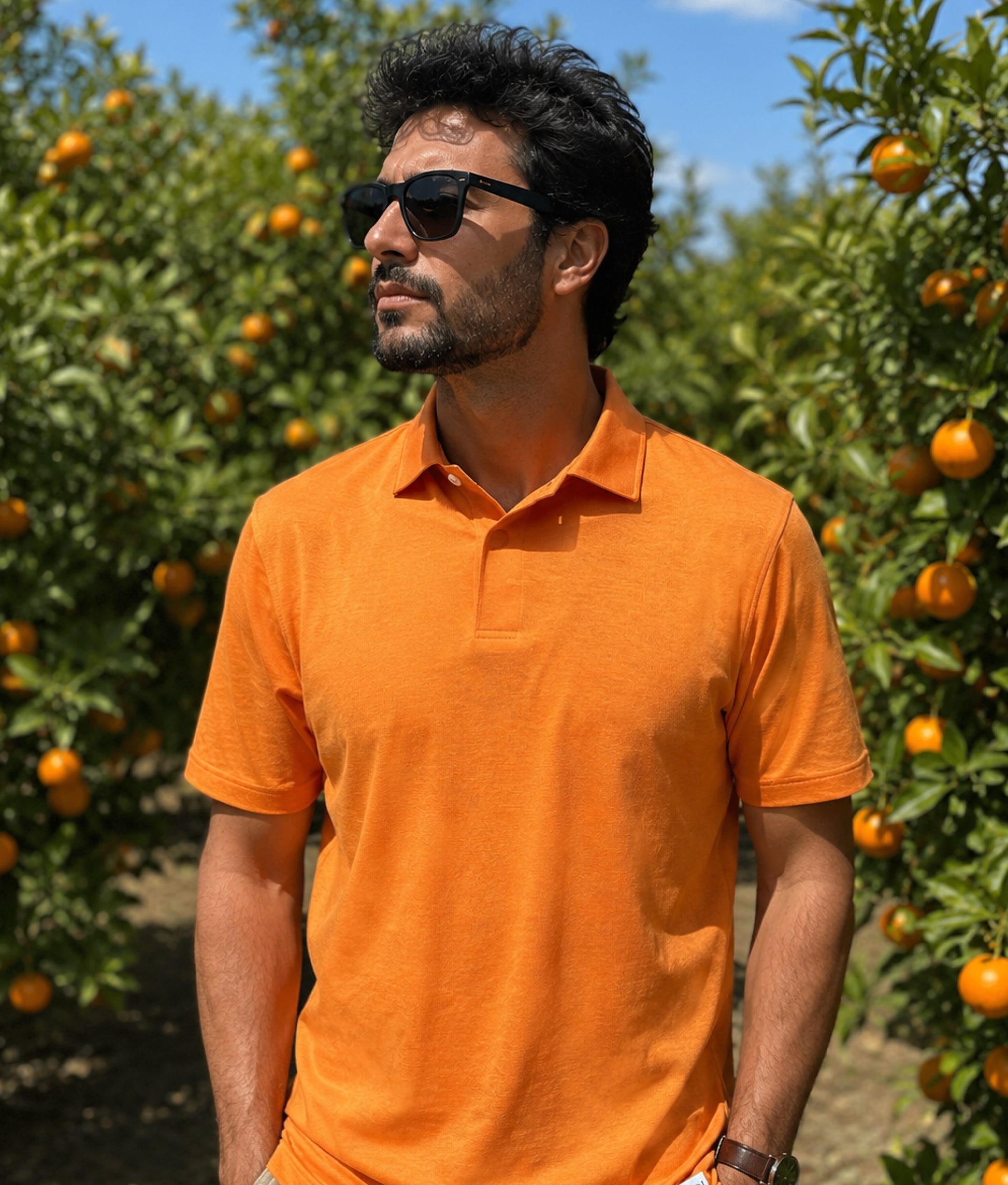 Man wearing an orange polo shirt and sunglasses standing in a grove of satsumas.