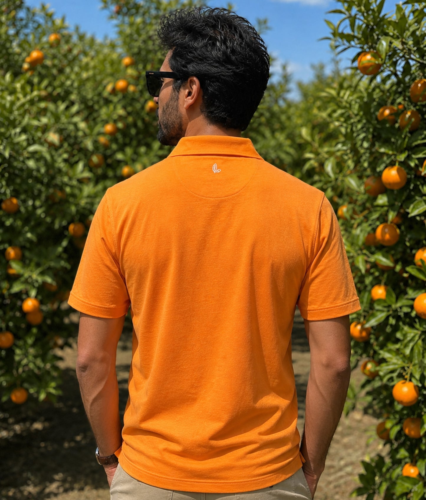 Man wearing an orange polo shirt and sunglasses standing in a grove of satsumas.