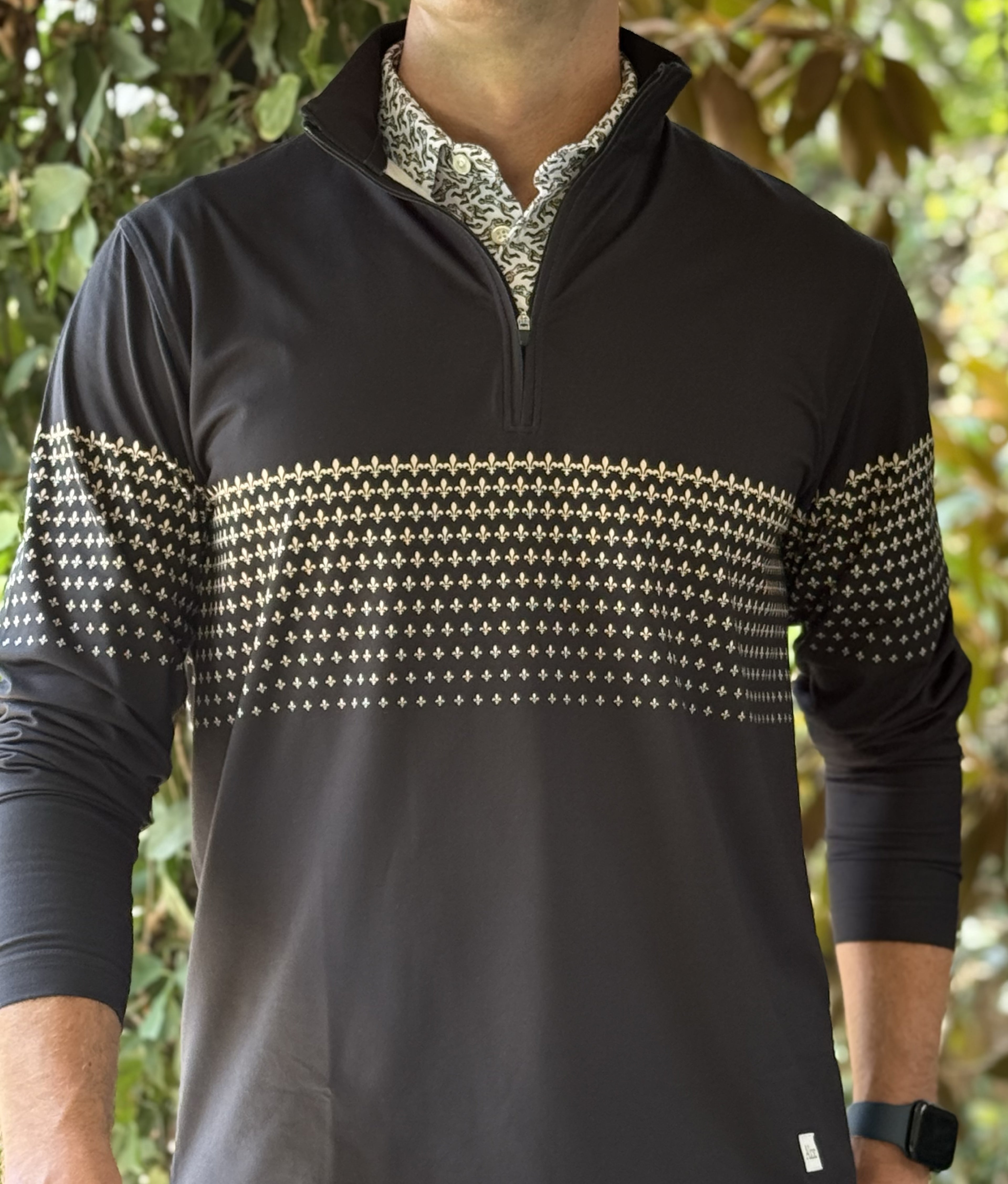 A man wearing a black quarter zip with a New Orleans Saints themed gold fleurs-de-lis pattern