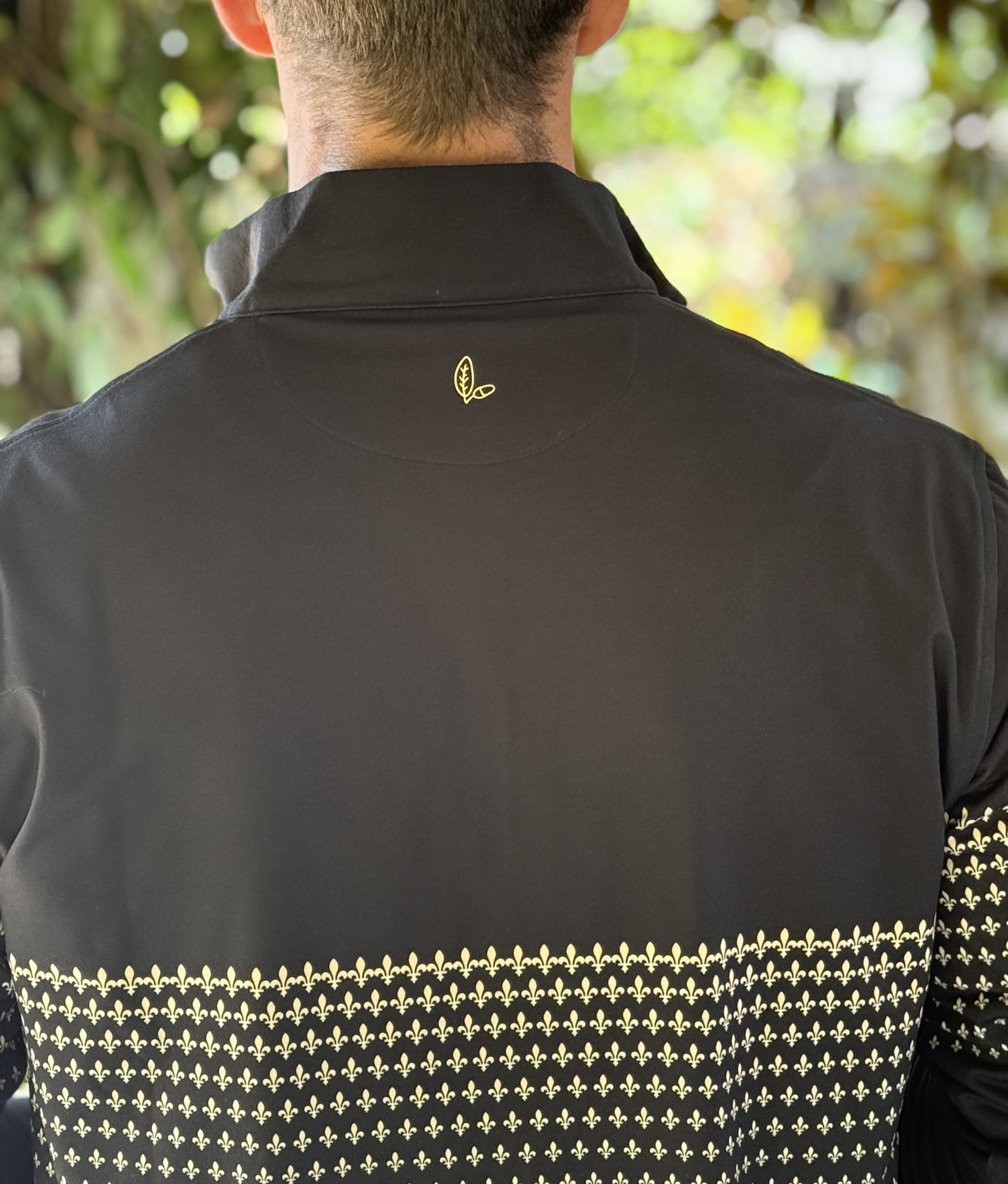 A man wearing a black quarter zip with a New Orleans Saints themed gold fleurs-de-lis pattern