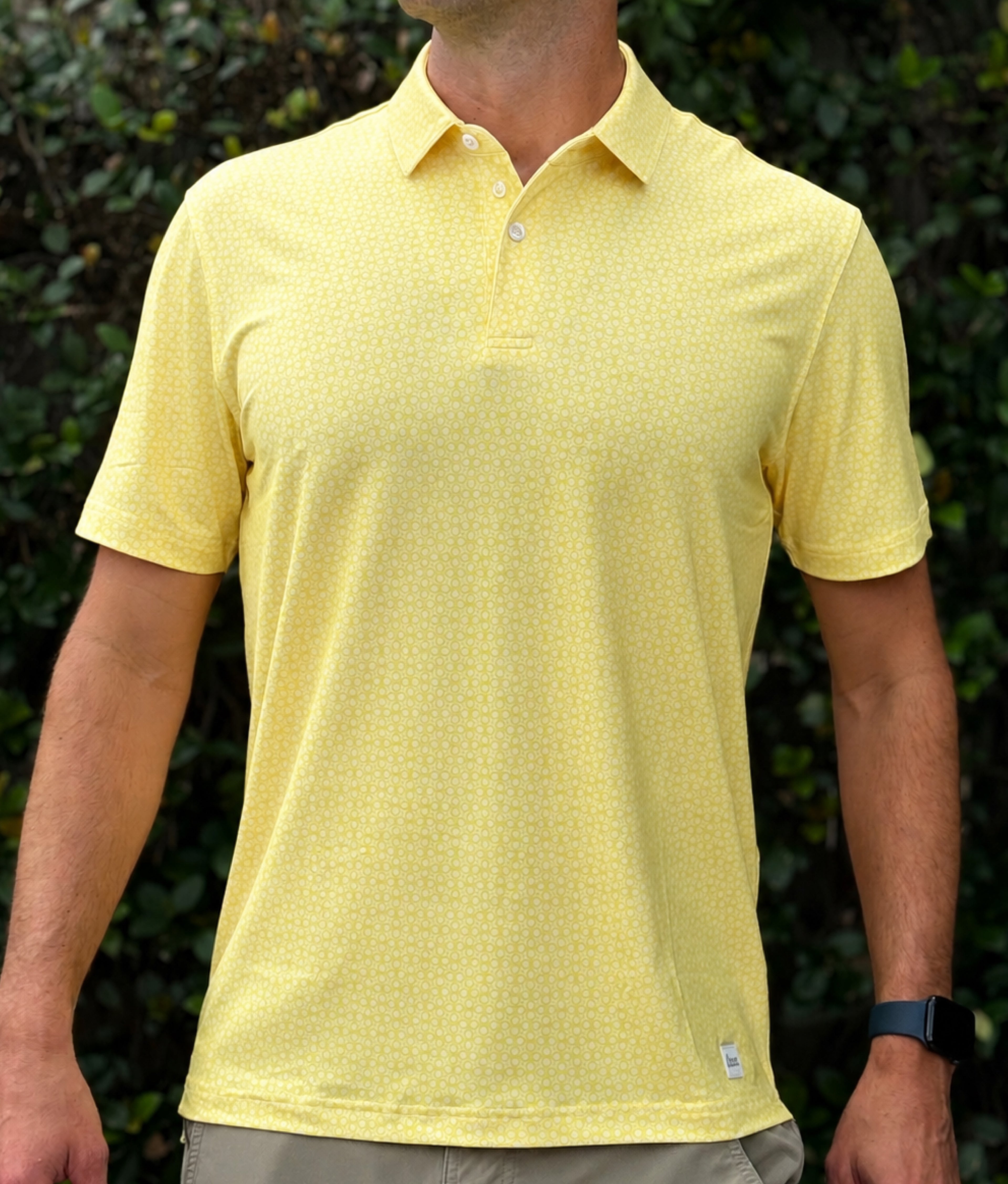 Person wearing a yellow patterned polo shirt with a blurred green background