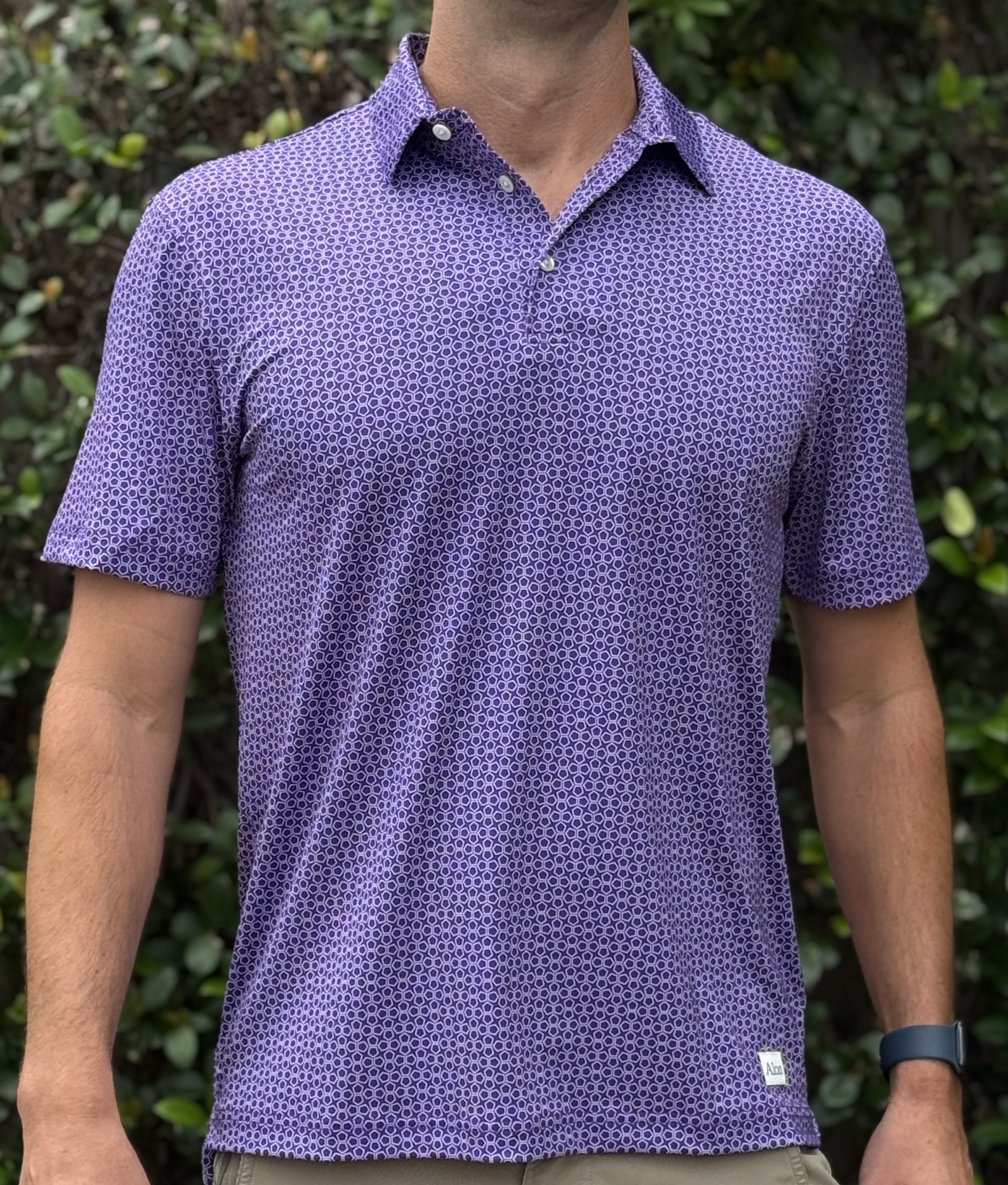 Man wearing a purple patterned polo shirt against a green leafy background