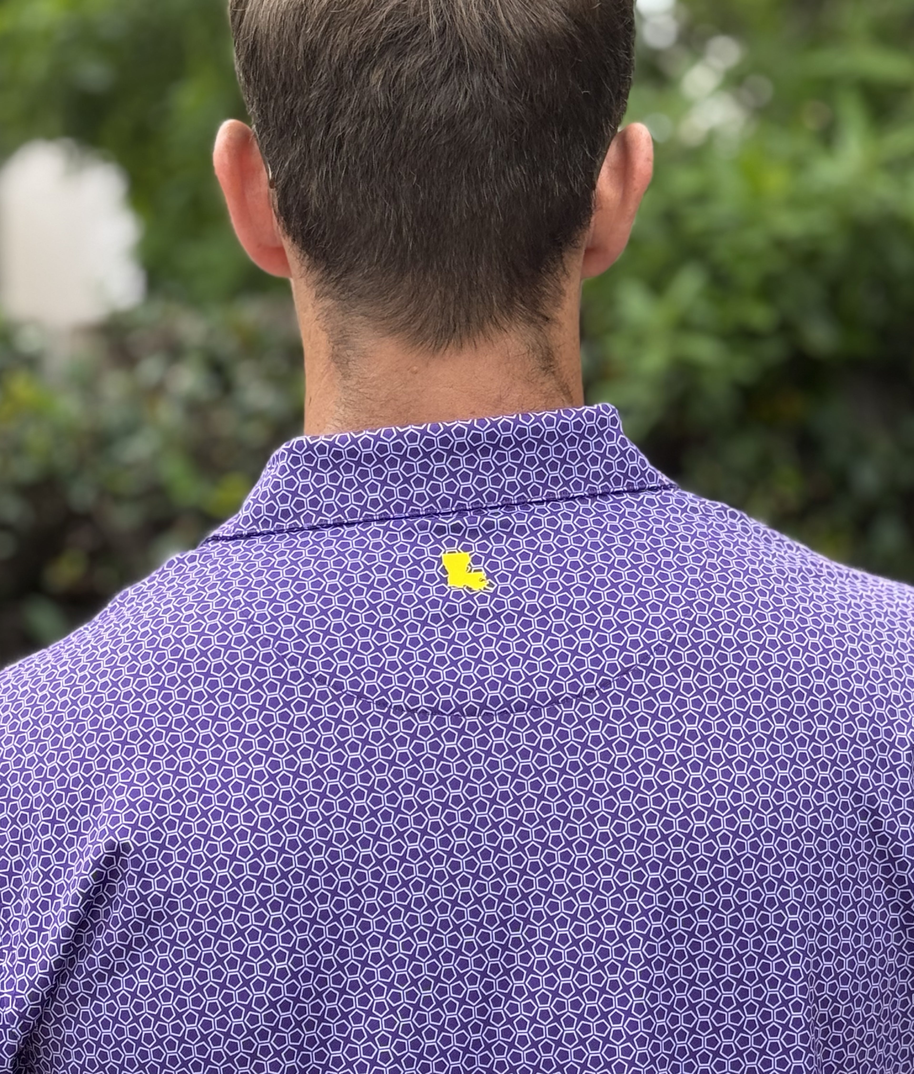Person wearing a purple patterned shirt with a yellow Louisiana logo, standing outdoors.