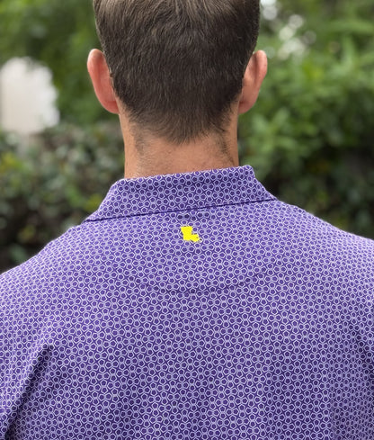 Person wearing a purple patterned shirt with a yellow Louisiana logo, standing outdoors.