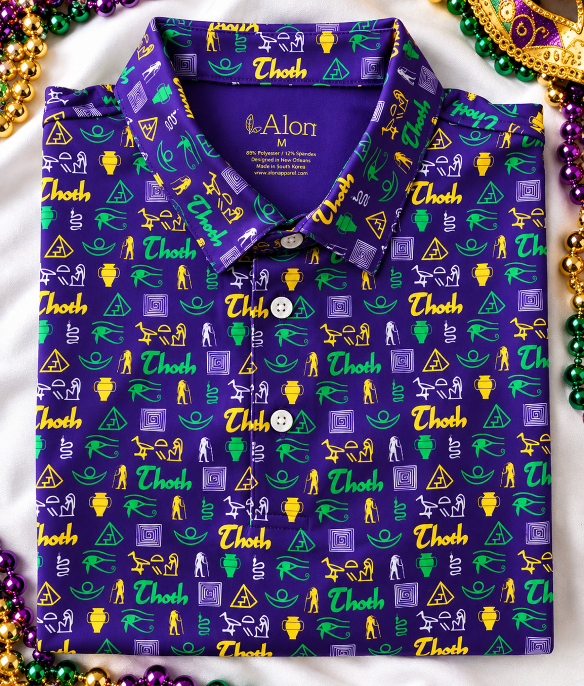 A folded polo shirt with a purple base and an all-over repeating pattern of green, gold, and lavender Thoth/Egyptian themed icons.