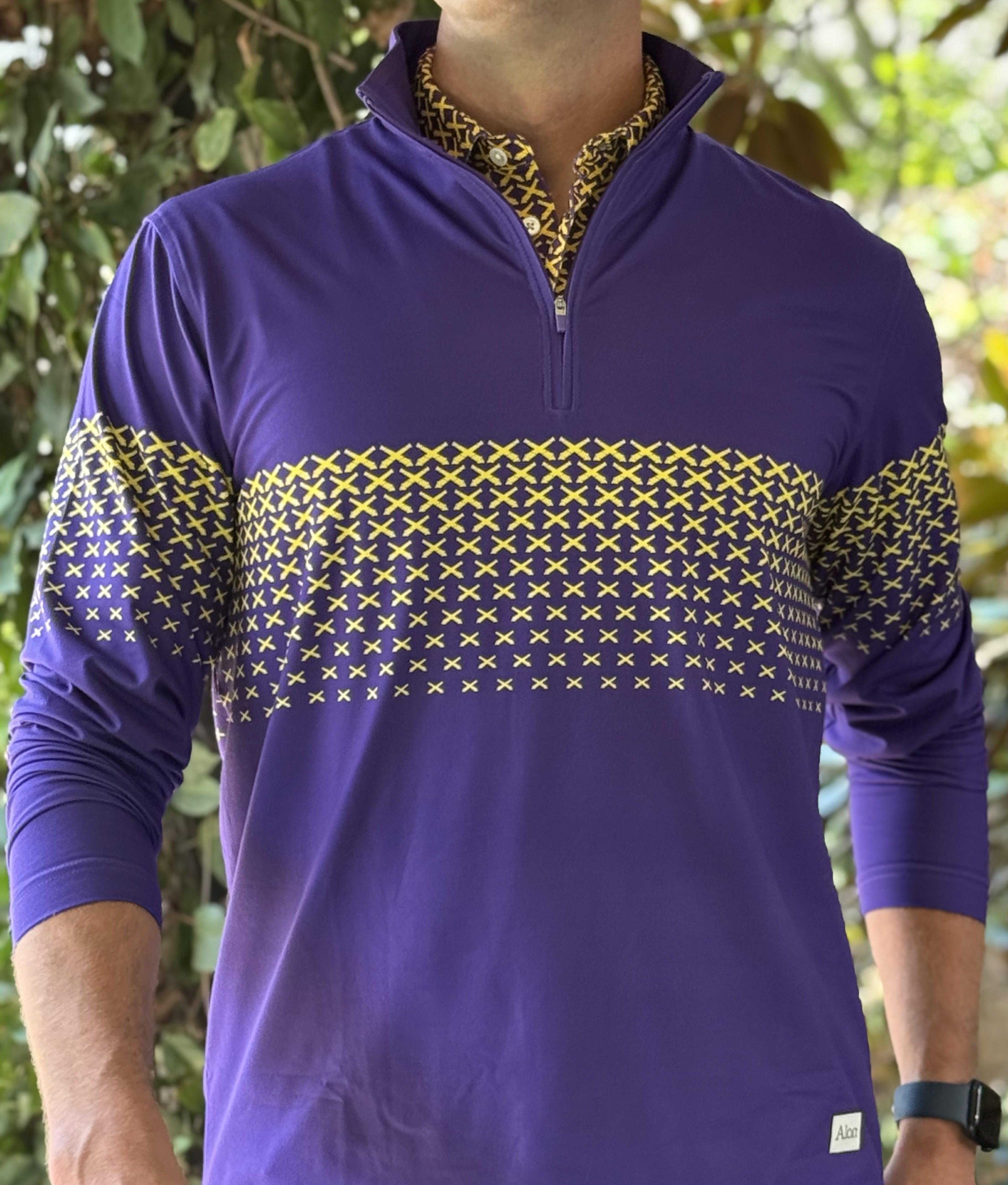 A man wearing a purple quarter zip with a gold LSU themed cannon pattern.