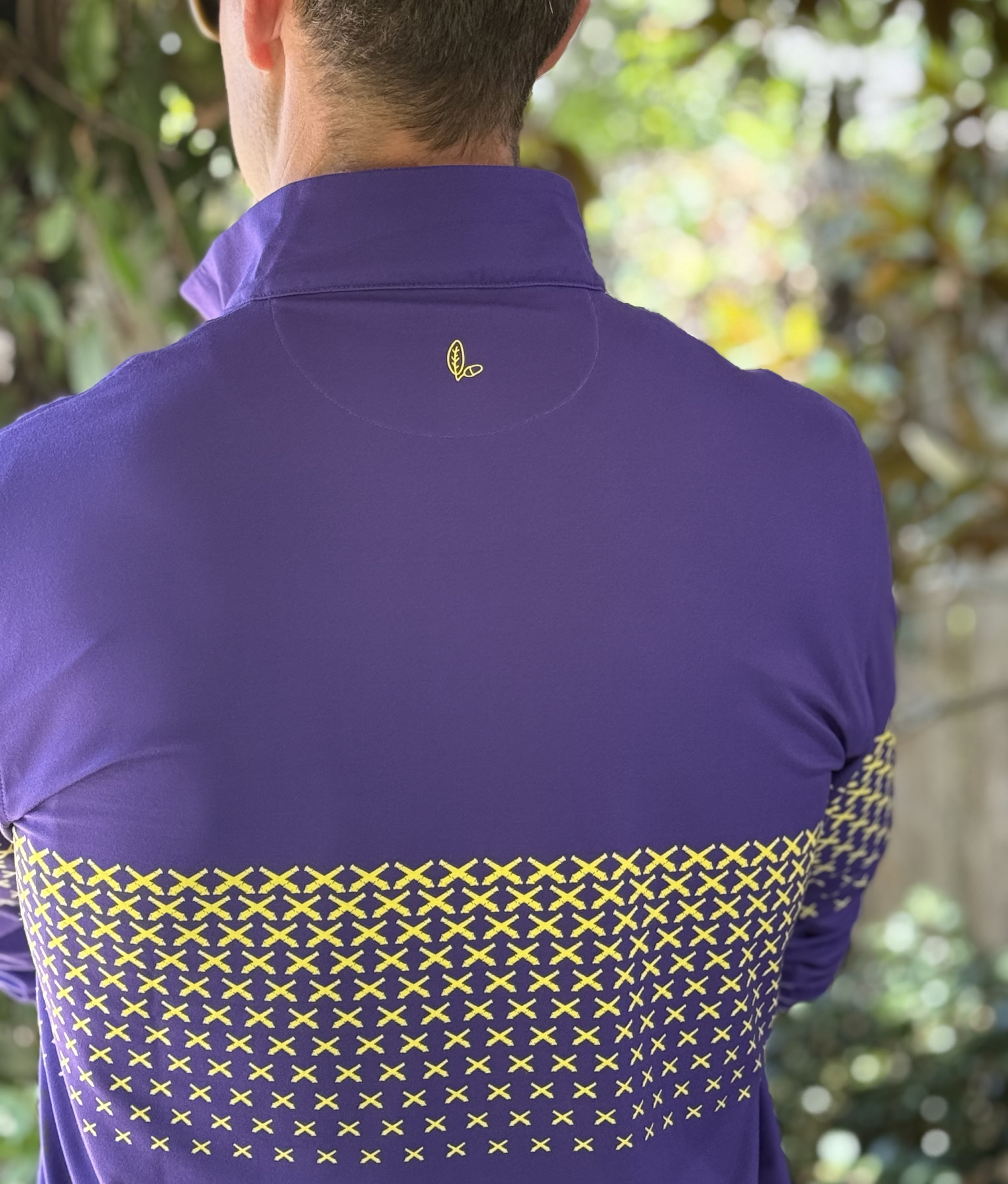 A man wearing a purple quarter zip with a gold LSU themed cannon pattern.