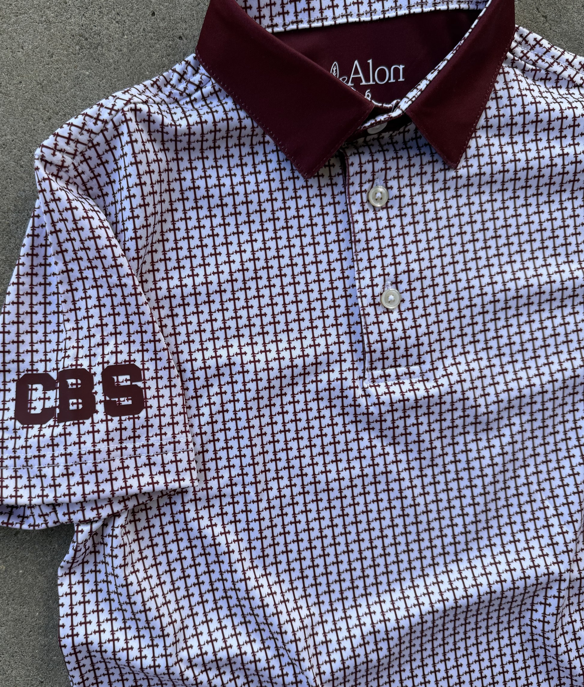 Crimson colored Lasallian cross patterned polo over white fabric with CBS heat transfer detail.